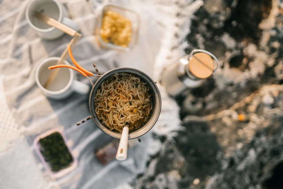 A pot of noodles and compact camp-cooking equipment arranged outdoors.