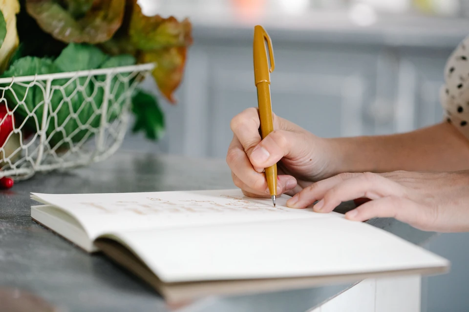 Hands writing in a notebook beside fresh produce.