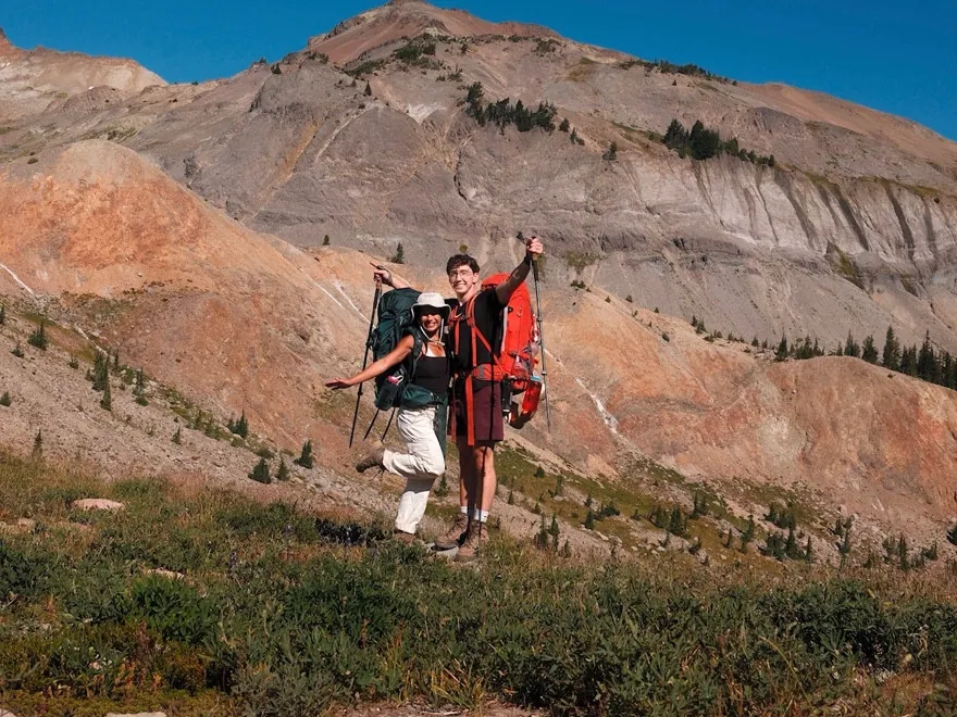 Two backpackers standing together on a mountain overlook, holding trekking poles.